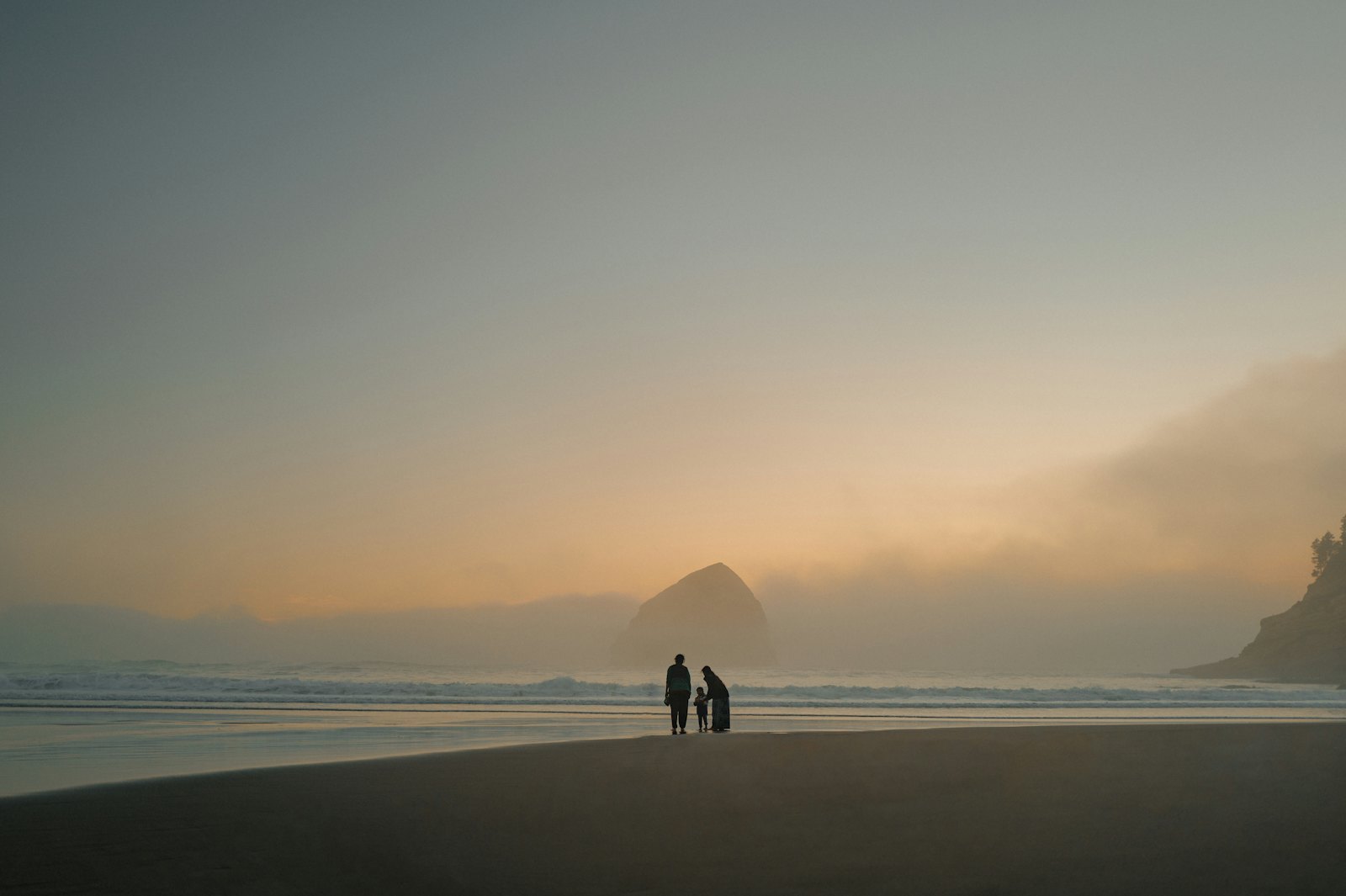 A family of three together on a misty beach at sunset