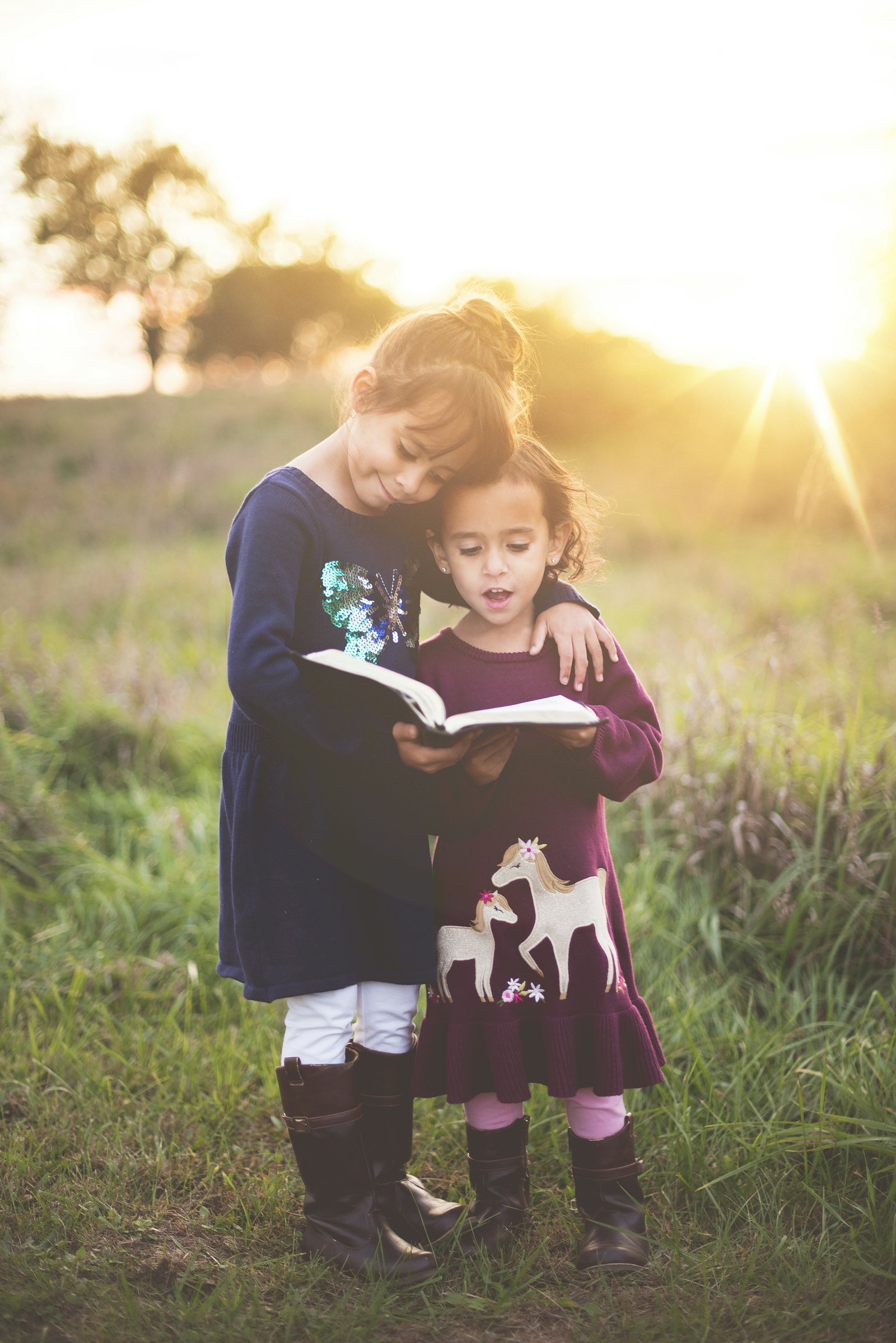 Two sisters sharing a book outdoors at golden hour