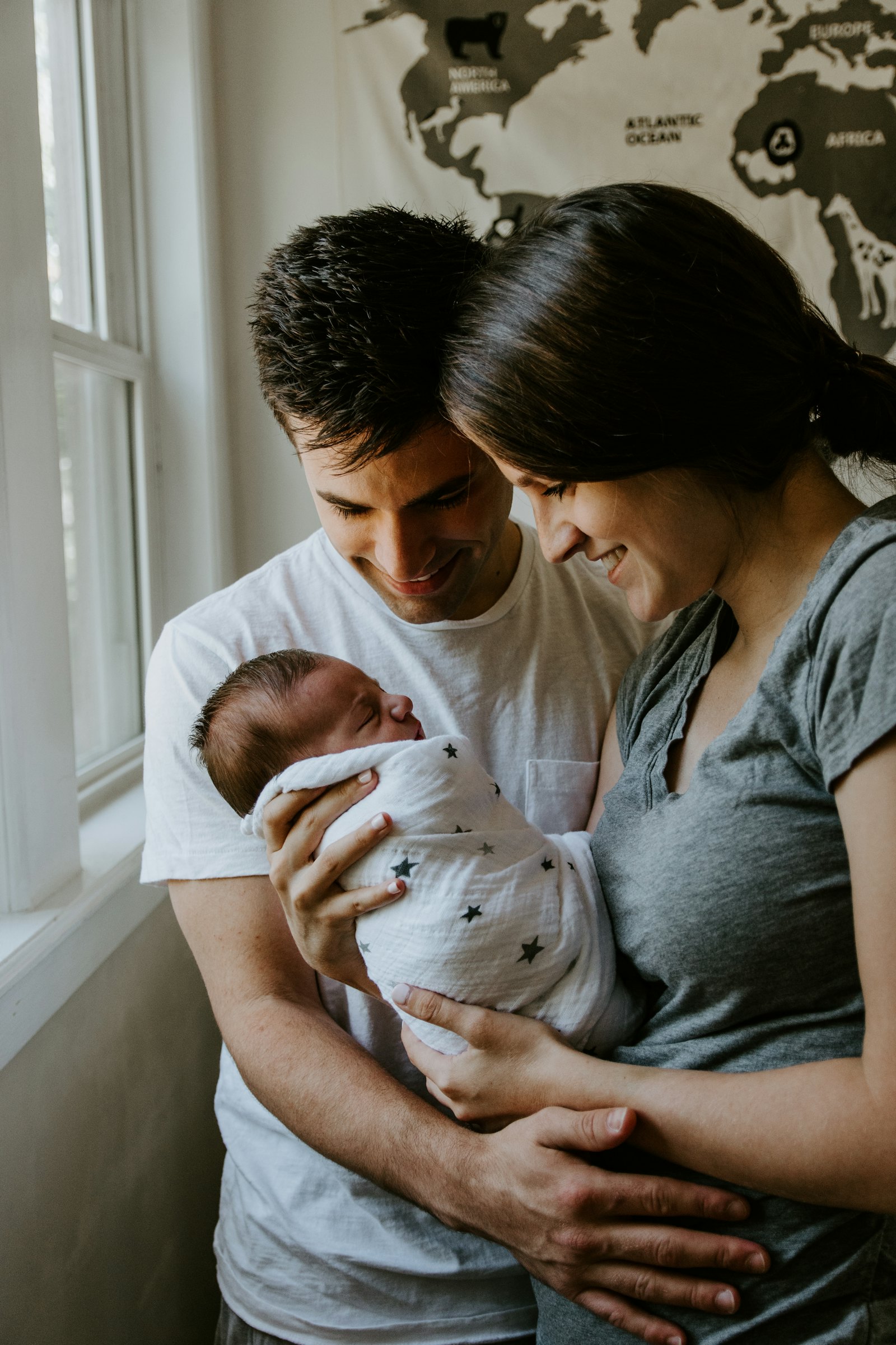 Parents holding their newborn in front of a world map